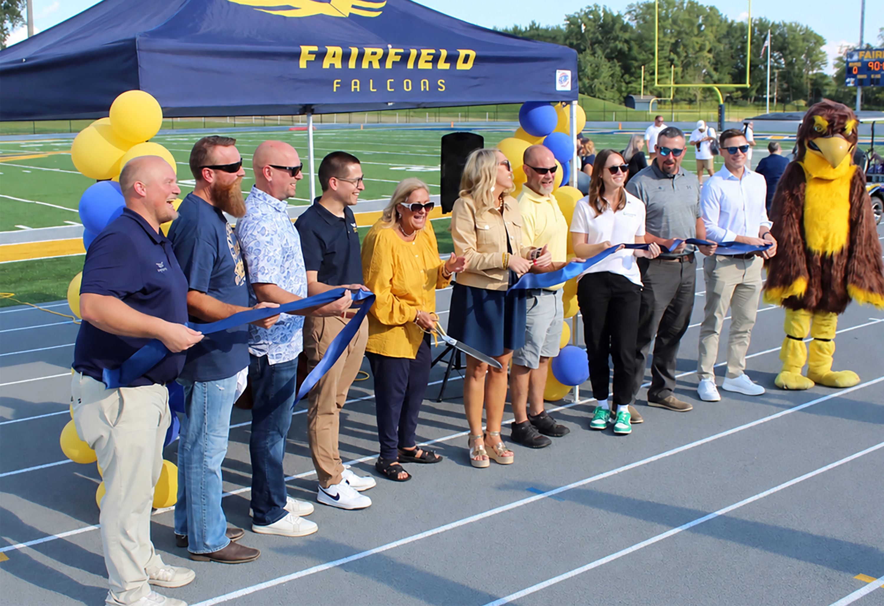 Fairfield Falcons ribbon-cutting ceremony on an athletic track, with people and mascot.